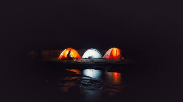 Colorful illuminated tents lined up along a dark lakeshore at night. Photo by Jimmy Liu