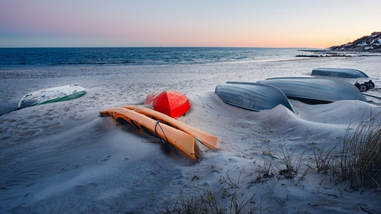Overturned wooden boats and a couple of kayaks resting on sandy beach at dusk. Tisvilde, Denmark. Photo by heino eisner