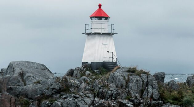 A white lighthouse on a rocky coast. Photo by Jamo Images